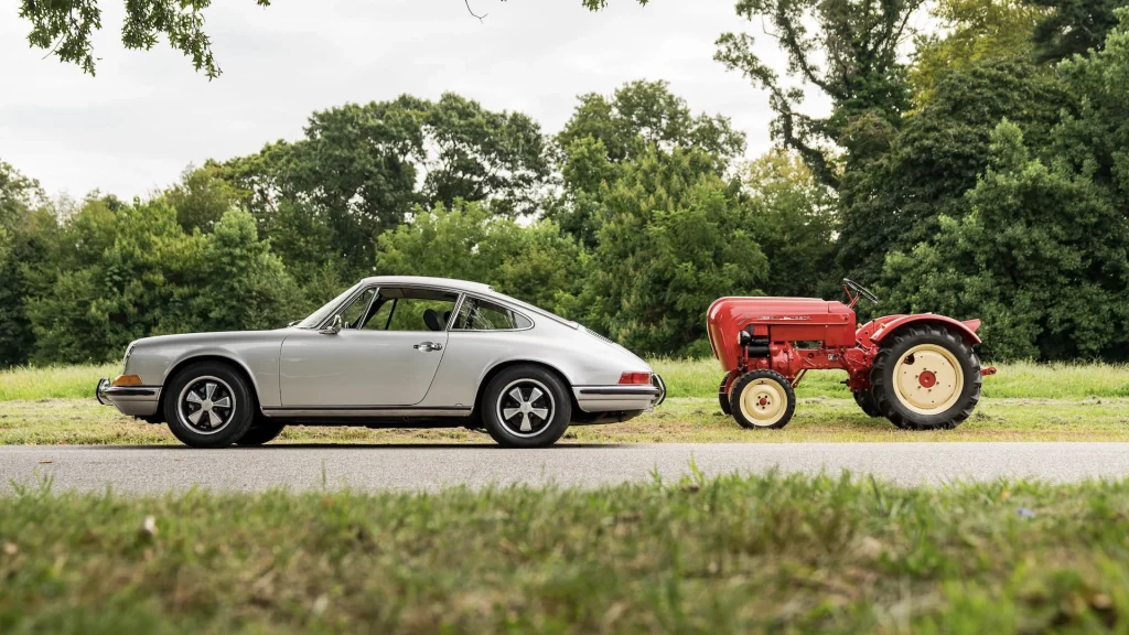 Silver Porsche and red Porsche tractor lined up on the side of a road