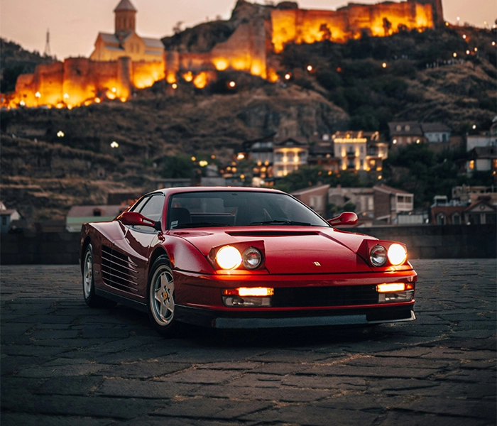 Red Ferrari Testarossa with city lights in the background